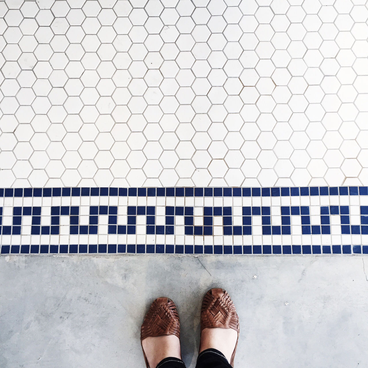 Foto de dois pés femininos sobre chão com ladrilhos decorativos.